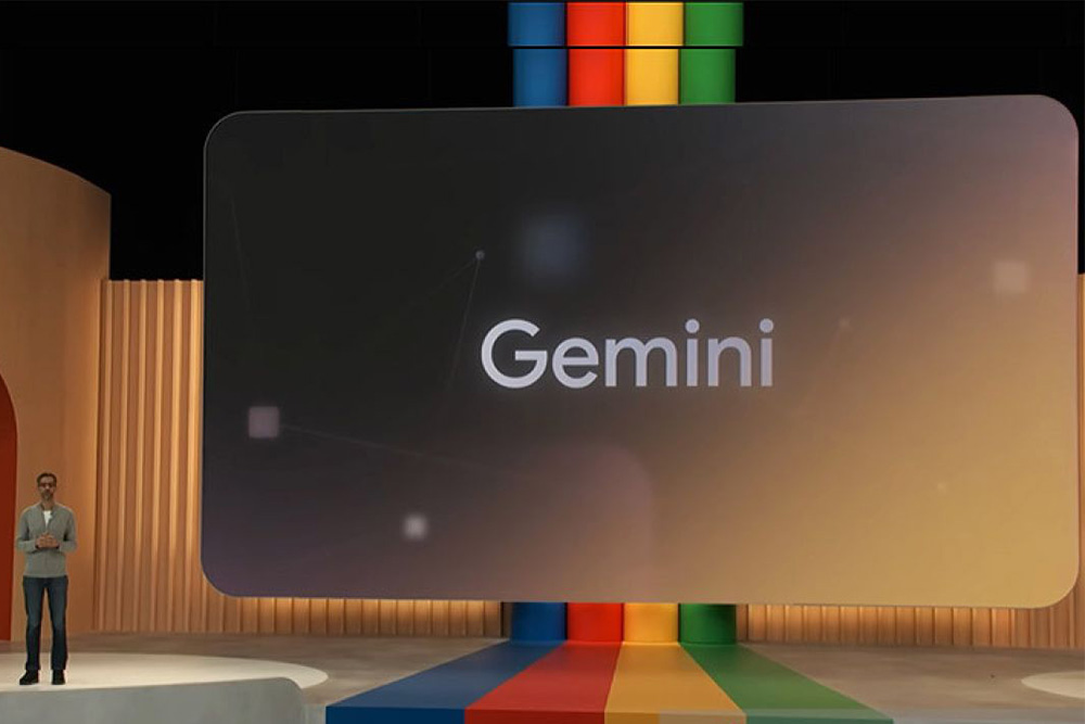 Google Gemini Logo auf einem Bildschirm bei einer Google-Veranstaltung projiziert mit einem Sprecher im Vordergrund, als Symbol für die Ankündigung und Verschiebung von Google Gemini.