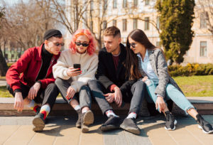 Bild zeigt junge Erwachsene auf einer Wiese, die gemeinsam auf einem Handy gucken. Es soll die auf Generation Z ausgerichtete E-Commerce Strategie andeuten.