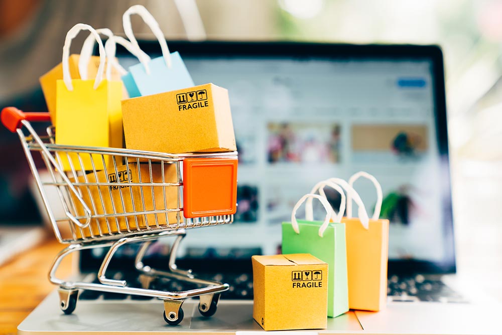 Das Bild zeigt einen vollen Einkaufswagen vor einem Laptop, symbolisierend, wie man einen Onlineshop erfolgreich macht.
